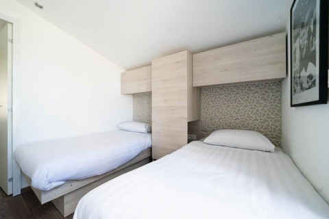 Hébergement glamping moderne avec deux lits simples, meubles en bois clair et décoration murale géométrique.