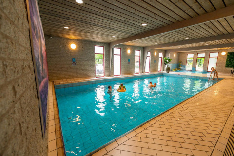 Piscina cubierta en un alojamiento glamping, niños jugando en el agua, ventanas grandes y ambiente acogedor.