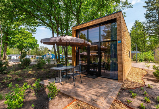 Moderne Tiny House lodge med træbeklædning, stor glasfacade og terrasse med havebord og parasol.