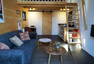 Interior de tiny house en De Hooge Veluwe, Países Bajos, con entrepiso, sofá y decoración de madera.