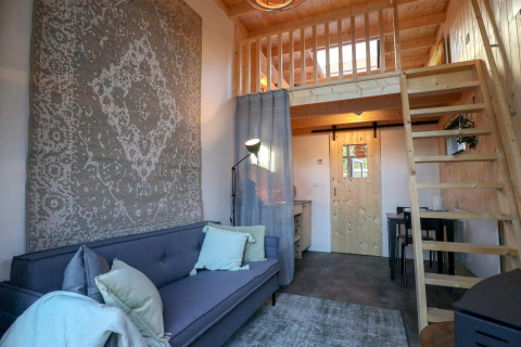 Vue intérieure du Tiny House à De Hooge Veluwe aux Pays-Bas avec mezzanine, canapé et décor en bois.