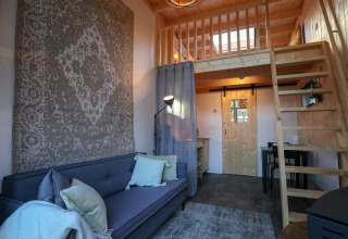 Vista interior de la Tiny House en De Hooge Veluwe, Países Bajos, con loft, sofá y decoración de madera.