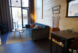 Acogedora sala en una Tiny House en De Hooge Veluwe, Países Bajos, con sofá, mesa y grandes ventanas.