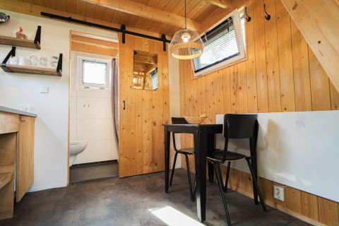 Lyst interiør i Tiny House ved De Hooge Veluwe i Holland med trævægge, spisebord og skydedør til badeværelse.