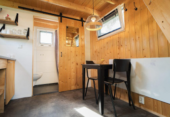 Lyst interiør i Tiny House ved De Hooge Veluwe i Holland med trævægge, spisebord og skydedør til badeværelse.