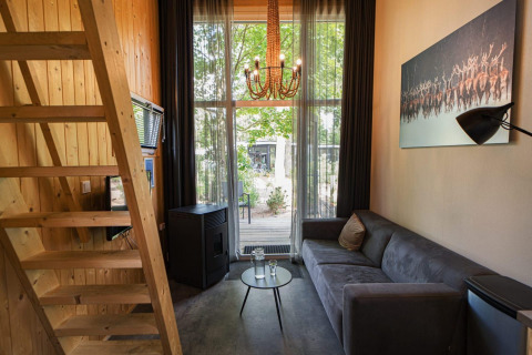 Interior moderno de una Tiny House lodge en De Hooge Veluwe, Países Bajos, con sofá, paredes de madera y gran ventana.