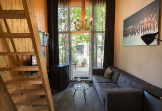 Interior moderno de una Tiny House lodge en De Hooge Veluwe, Países Bajos, con sofá, paredes de madera y gran ventana.