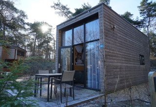 Moderne houten tiny house lodge bij De Hooge Veluwe in Nederland, met terras en zitjes in het bos.