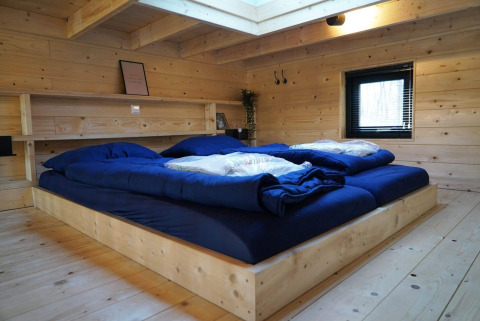 Soveværelse i Tiny House ved De Hooge Veluwe med trævægge, stort seng og naturligt lysindfald.