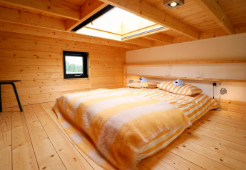 Knusse slaapkamer met houten wanden, dakraam en gestreept beddengoed in Tiny House bij De Hooge Veluwe.