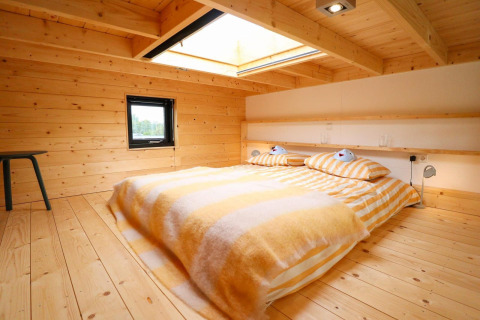 Et hyggeligt soveværelse med trævægge, stort ovenlysvindue og stribede senge på Tiny House at De Hooge Veluwe.