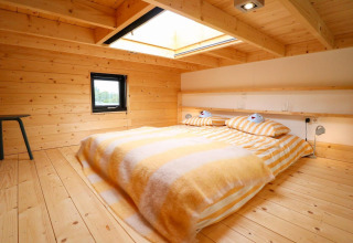 Et hyggeligt soveværelse med trævægge, stort ovenlysvindue og stribede senge på Tiny House at De Hooge Veluwe.
