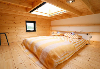 Et hyggeligt soveværelse med trævægge, stort ovenlysvindue og stribede senge på Tiny House at De Hooge Veluwe.