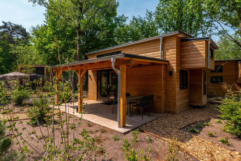 Moderna cabaña Tiny House de madera en el bosque, terraza techada y comedor al aire libre con sillas