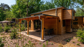 Moderne Tiny House lodge i skoven med træfacade, overdækket terrasse og havemøbler i solskin