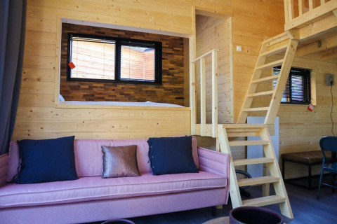 Interiør af en Tiny House-lodge ved De Hooge Veluwe i Holland med trævægge og en lyserød sofa.