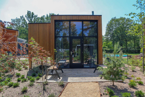 Moderne Tiny House-lodge med store glasvinduer, træfacade og grøn have ved De Hooge Veluwe, Holland.