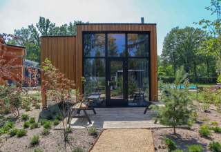 Moderne Tiny House-lodge med store glasvinduer, træfacade og grøn have ved De Hooge Veluwe, Holland.