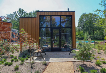 Moderne Tiny House-lodge med store glasvinduer, træfacade og grøn have ved De Hooge Veluwe, Holland.
