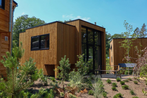 Tiny House moderne au lodge De Hooge Veluwe aux Pays-Bas, façade bois, entourée de verdure et ciel bleu.