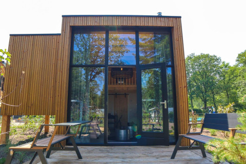 Moderne Tiny House-lodge med store vinduer og terrasse ved De Hooge Veluwe i Holland, omgivet af natur.