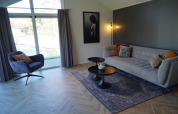 Salon moderne du lodge Velthorst à De Hooge Veluwe, Pays-Bas, avec canapé, fauteuil et grande baie vitrée.