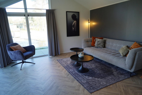 Salon moderne du lodge Velthorst à De Hooge Veluwe, Pays-Bas, avec canapé, fauteuil et grande baie vitrée.