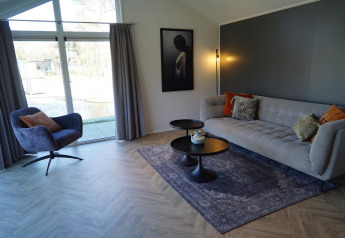 Salon moderne du lodge Velthorst à De Hooge Veluwe, Pays-Bas, avec canapé, fauteuil et grande baie vitrée.