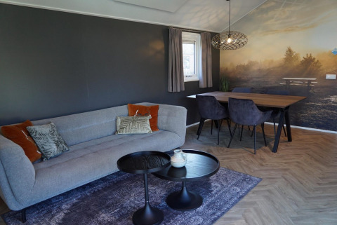 Salón moderno en el lodge Velthorst en De Hooge Veluwe, Países Bajos, con sofá, mesa y mural de paisaje.