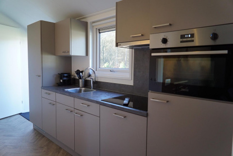 Cocina moderna en una cabaña Velthorst en De Hooge Veluwe, Países Bajos, con horno y ventana grande.
