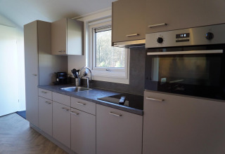Intérieur de cuisine moderne dans un lodge Velthorst à De Hooge Veluwe, Pays-Bas, avec four et fenêtre.