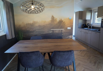 Dining area in Velthorst lodge at De Hooge Veluwe, Netherlands, featuring scenic wall art and kitchen.