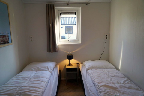 Deux lits simples avec du linge blanc dans une chambre basique du lodge Velthorst à De Hooge Veluwe, Pays-Bas.