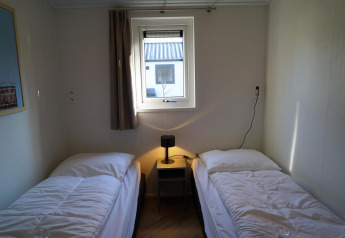 Twee enkele bedden met wit beddengoed in een eenvoudige kamer van Velthorst lodge, De Hooge Veluwe, Nederland.