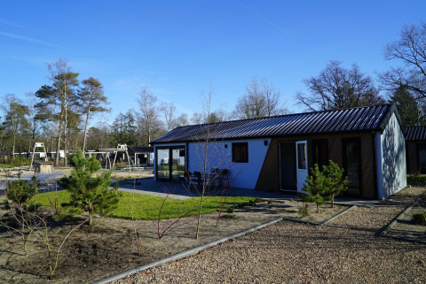 Lodge Velthorst moderne à De Hooge Veluwe aux Pays-Bas entouré d’arbres et d’une aire de jeux.