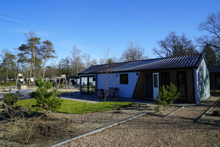 Lodge moderno Velthorst en De Hooge Veluwe, Países Bajos, con área verde y columpios en el fondo.