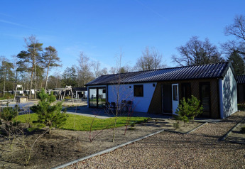 Lodge Velthorst moderne à De Hooge Veluwe aux Pays-Bas entouré d’arbres et d’une aire de jeux.