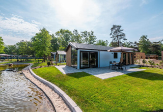 Moderne Lodge mit Terrasse und Sonnenschirm in De Hooge Veluwe, Niederlande, neben einem Teich gelegen.