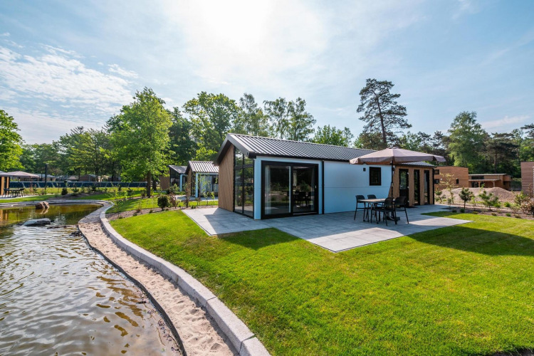 Lodge moderno con terraza y sombrilla en De Hooge Veluwe, Países Bajos, junto a un estanque en naturaleza.