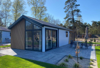 Lodge Velthorst moderne à De Hooge Veluwe, Pays-Bas, avec terrasse, grandes fenêtres et vue sur la forêt.