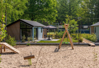 Modern lodges at Velthorst De Hooge Veluwe, Netherlands, featuring a playground and lush greenery.