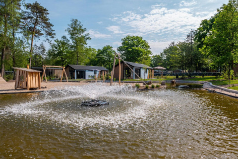 Außenansicht der Velthorst Lodge im De Hooge Veluwe, Niederlande, mit Teich und Springbrunnen im Vordergrund.