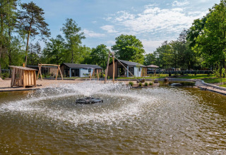 Außenansicht der Velthorst Lodge im De Hooge Veluwe, Niederlande, mit Teich und Springbrunnen im Vordergrund.