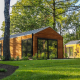 Wellness Lodge ved De Hooge Veluwe i Holland, omgivet af frodige grønne træer og velplejet græsplæne.