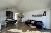 Modern stue i Forest Lodge ved De Hooge Veluwe, Holland, med spisebord, blå sofa og åbent køkken.