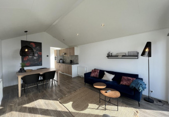 Lichte woonkamer bij Forest Lodge in De Hooge Veluwe, Nederland, met eettafel, blauwe bank en keuken.