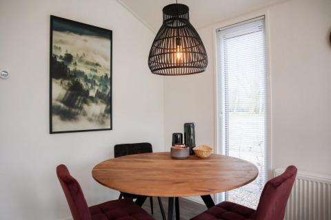 Spisehjørne i Forest Lodge ved De Hooge Veluwe, Holland, med rundt træbord, moderne lamper og naturbillede.