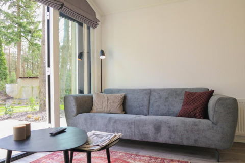 Heldere woonkamer in Forest Lodge, De Hooge Veluwe, Nederland, met grijze zetel en uitzicht op bos.