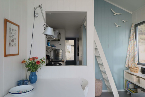 Interior luminoso y acogedor de Beach house 'Dishoek 60' con flores, pared azul y ventana hacia la cocina.