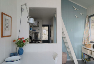 Intérieur lumineux et chaleureux de Beach house 'Dishoek 60' avec fleurs, panneau bleu et vue cuisine.